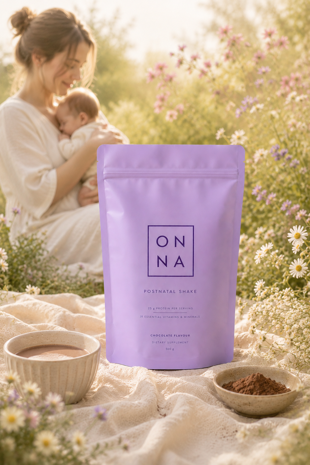 Mother holding her newborn beside an ONNA Postnatal Shake pouch in a sunlit meadow